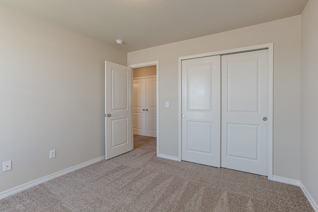 Empty bedroom with sliding closet doors, open entry door, and carpeted flooring.