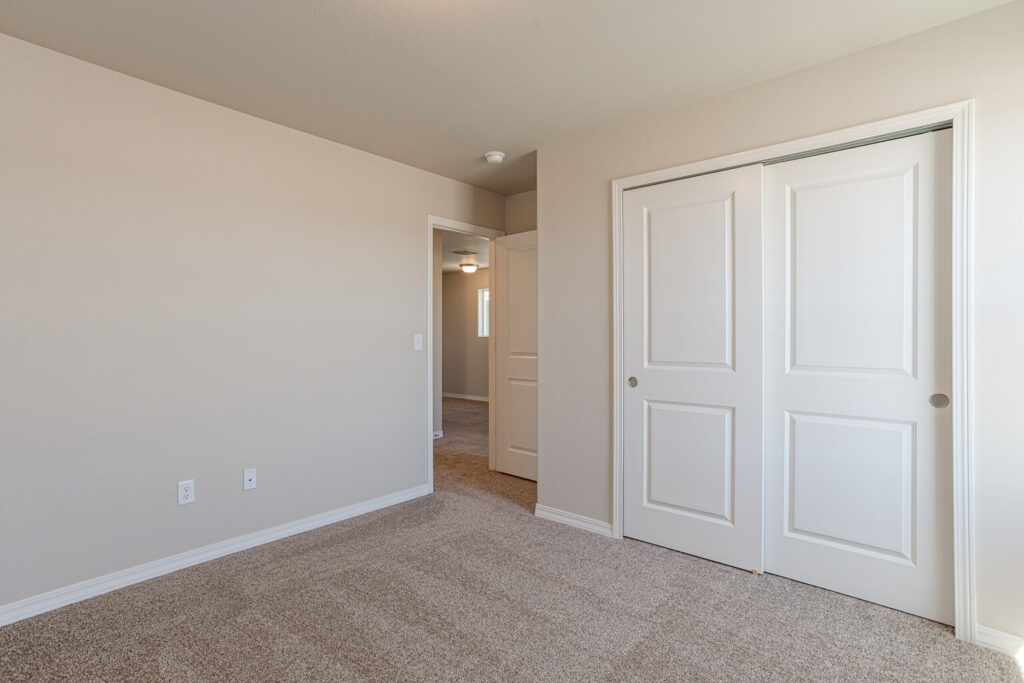 Neutral painted bedroom interior with sliding closet doors and open doorway to a hallway.