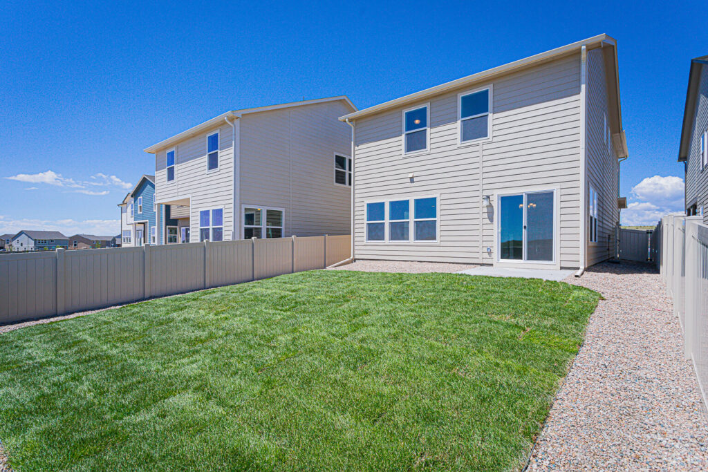 Backyard with green lawn, gravel side paths and two-story siding house with sliding glass door.