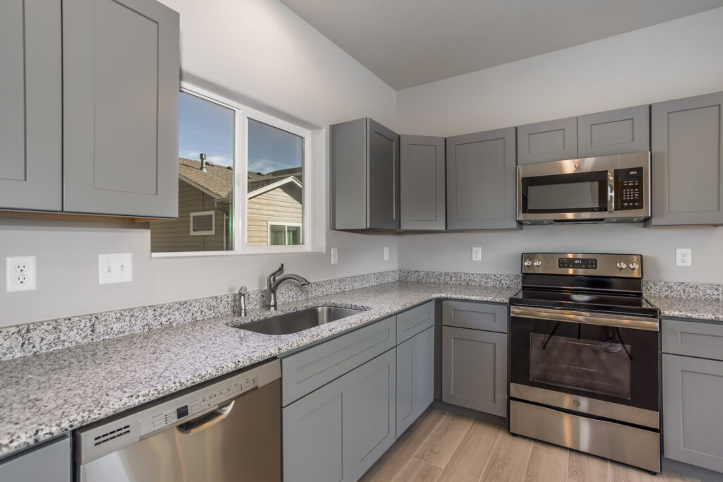 Modern kitchen with gray shaker cabinets, speckled granite countertops, and stainless appliances.