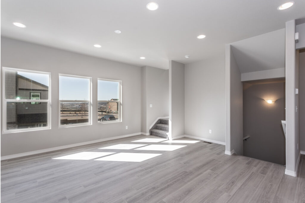 Bright, open living area with three windows, light gray floors, and stairs leading down.