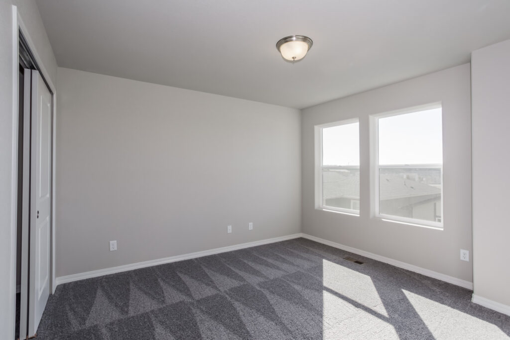Empty bedroom with patterned gray carpet, two windows, and a closet with sliding doors.