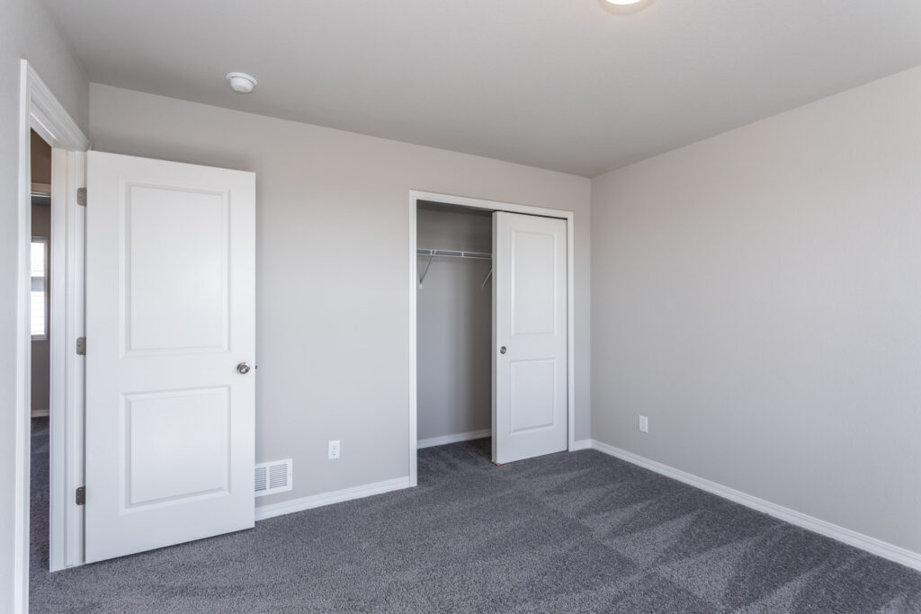 Empty bedroom with open closet and white door, gray carpet and neutral walls.
