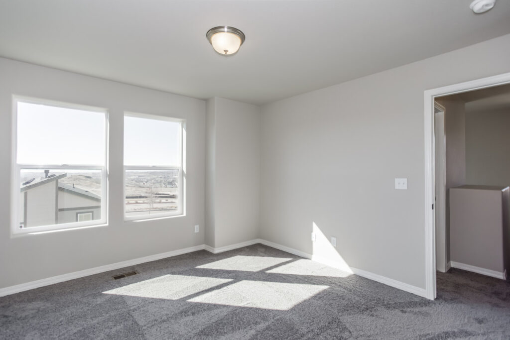 Bedroom with two side-by-side windows, neutral walls and patterned gray carpet.