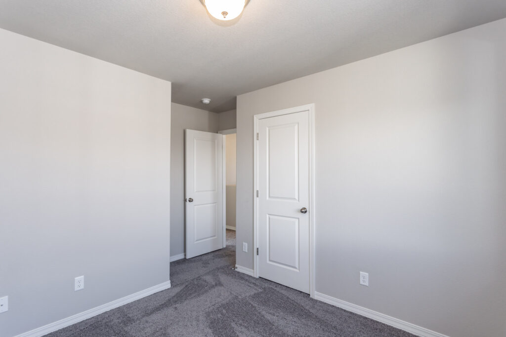 Empty room corner with two white doors, gray carpet and a ceiling light fixture.