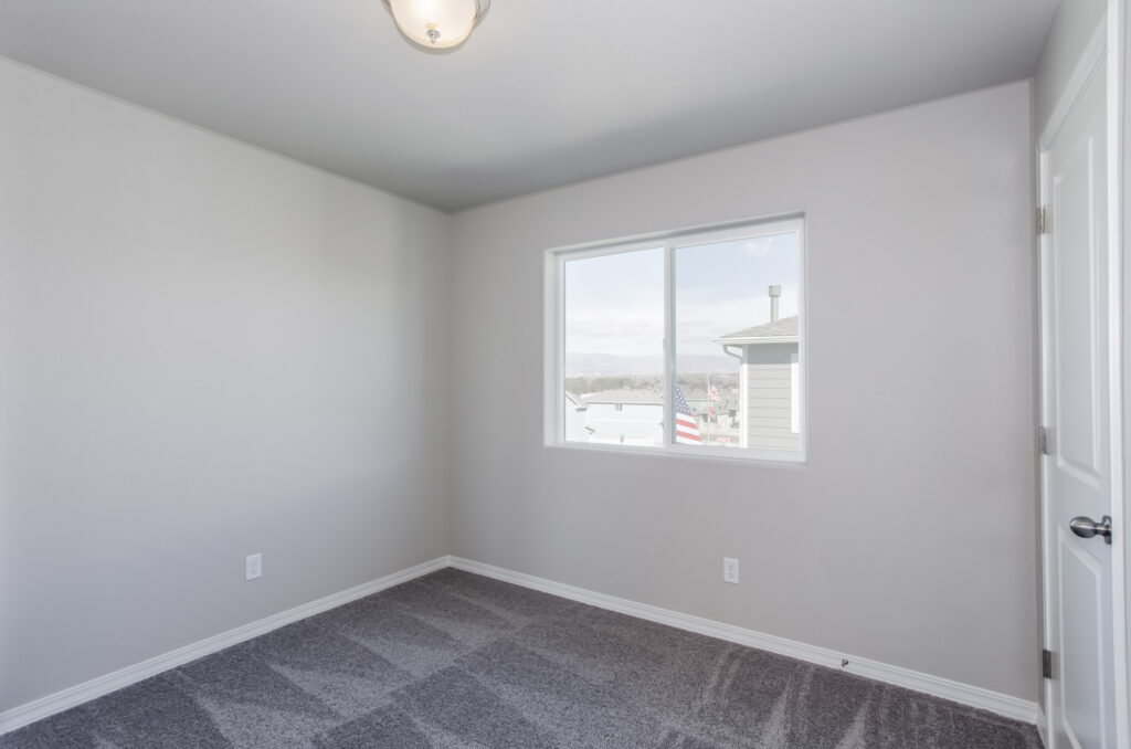 Unfurnished room with a single window overlooking nearby houses and gray carpet.