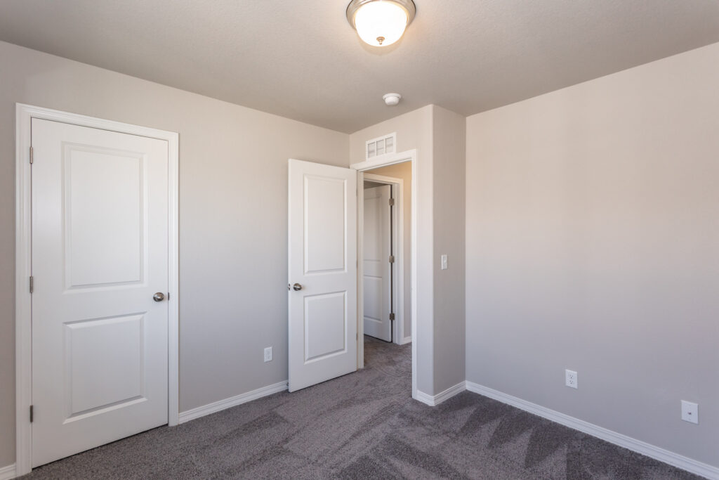 Empty bedroom with gray carpet, light gray walls, and two white doors.