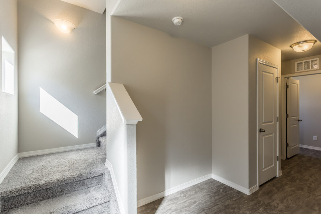 Carpeted stair landing with short half-wall and hallway leading to closed doors.