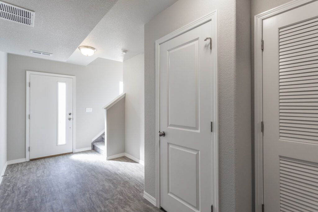 Bright entryway with front door, small stairwell, gray flooring, and interior doors.