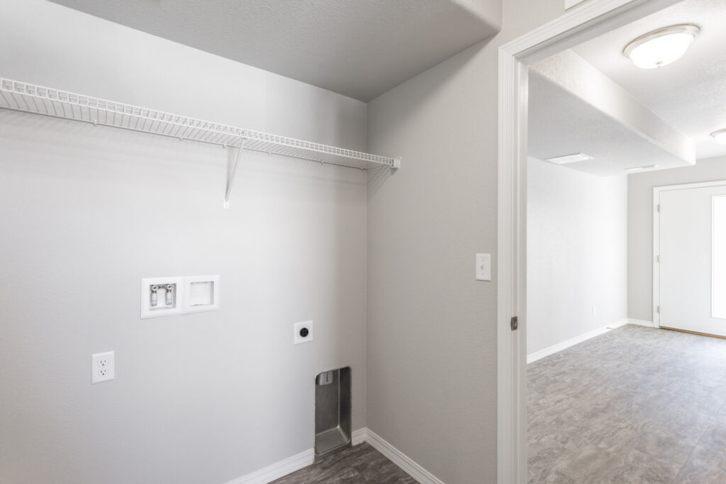 Small laundry alcove with wire shelf, washer/dryer hookups and gray flooring.