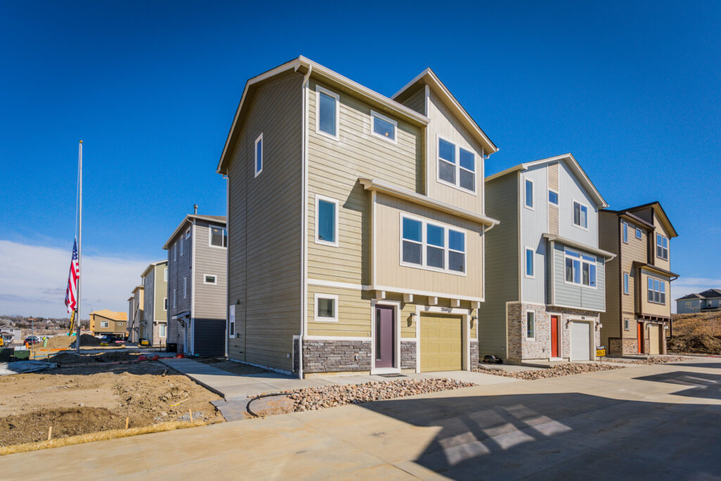 Row of narrow three-story modern townhomes with garages and varied exterior colors.
