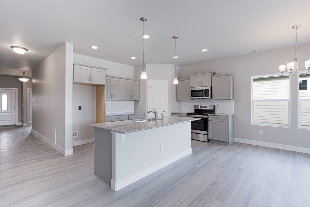 Open kitchen with central island, granite countertop, pendant lights, and light gray cabinetry.