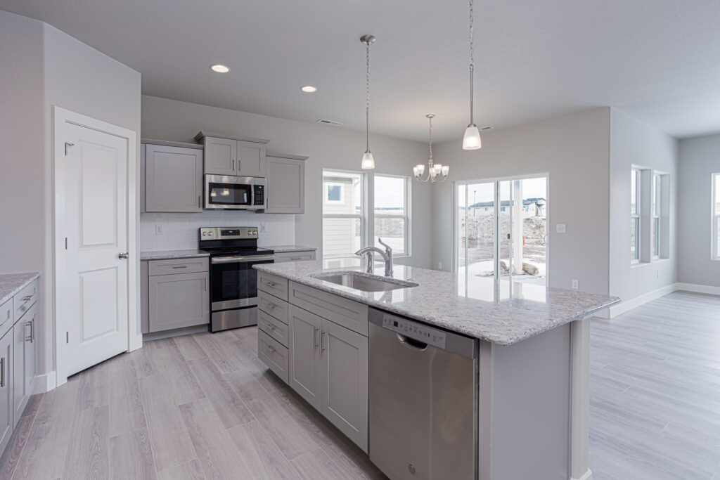 Kitchen island with sink and dishwasher, stove and microwave against the wall, dining area beyond.
