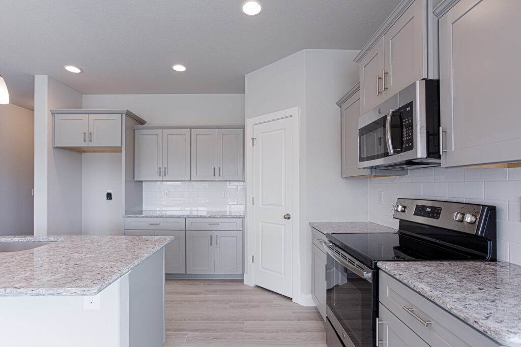 Kitchen angled view showing stovetop, microwave, pantry door, and countertop workspace.