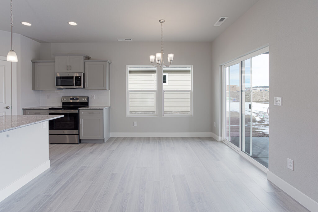 Open-plan kitchen and dining area with gray cabinets, stainless appliances, and sliding glass door.