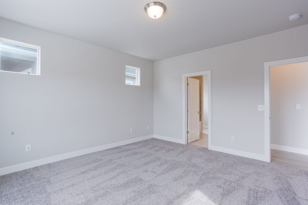 Empty carpeted bedroom with two small high windows and an open doorway to a bathroom.