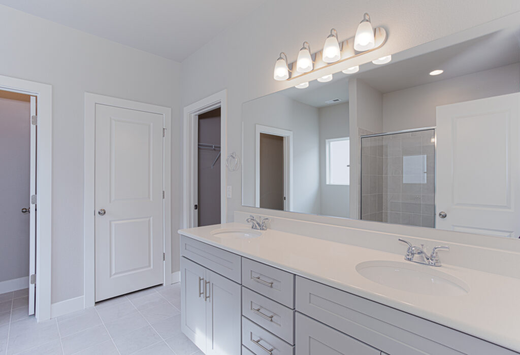 Bathroom vanity with double sinks, large mirror, and overhead light fixtures.