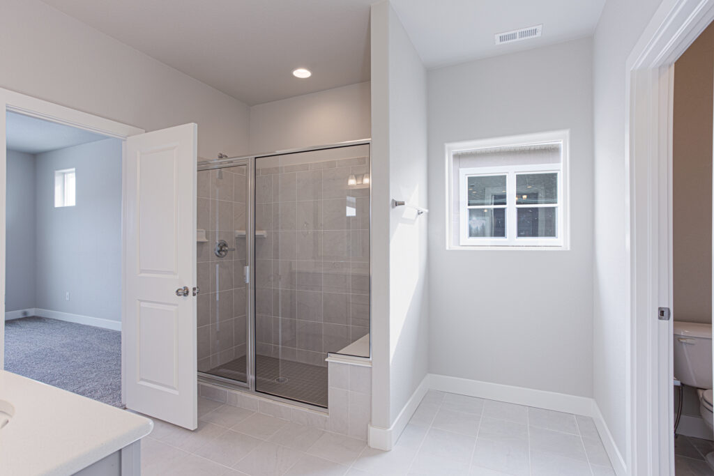 Bright bathroom with glass-enclosed tiled shower and small window beside it.