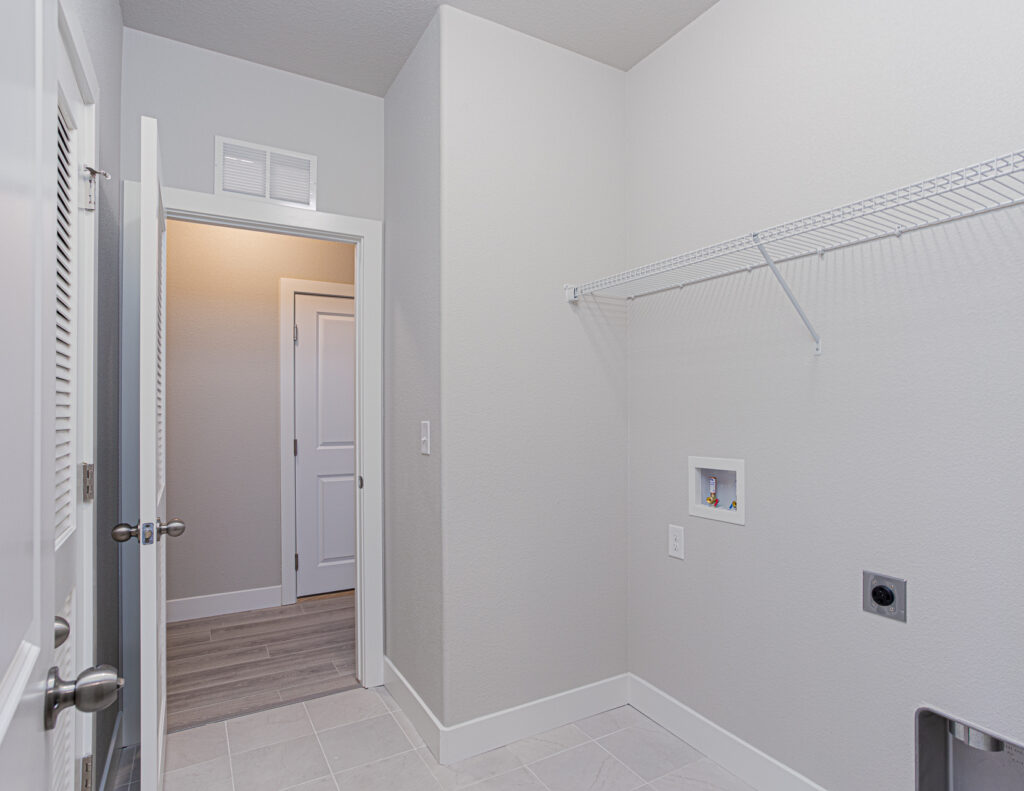 Laundry room with tiled floor, wall-mounted wire shelf, and washer/dryer hookups.