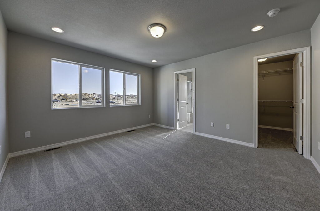 Empty carpeted bedroom with three-pane window and walk-in closet doorway.