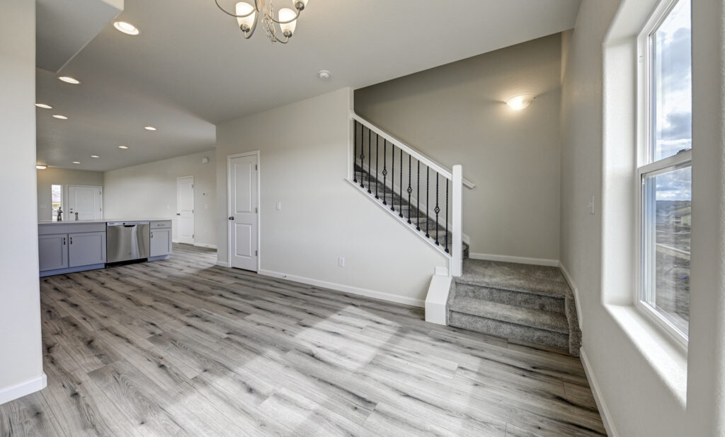 Open living area with a view of the kitchen, staircase with carpeted steps and decorative railing.