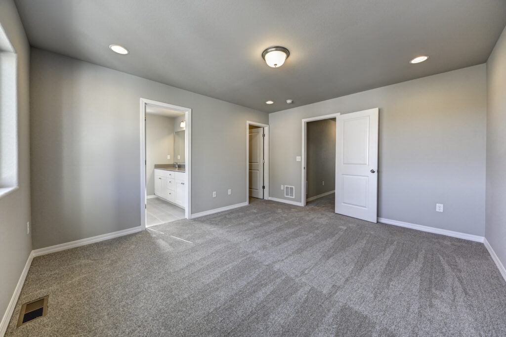 Spacious carpeted room showing doorways to a bathroom and hallway.
