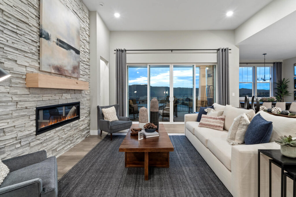 Living room with stone fireplace, sliding glass doors, and neutral seating arranged around a wood table.
