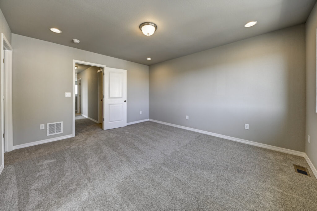 Empty rectangular room with gray carpet and closed white door.