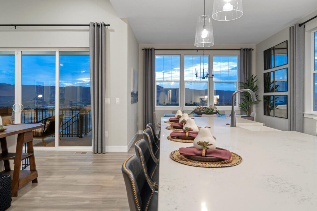 Kitchen island with bar seating, place settings, and large windows showing a dusk view.