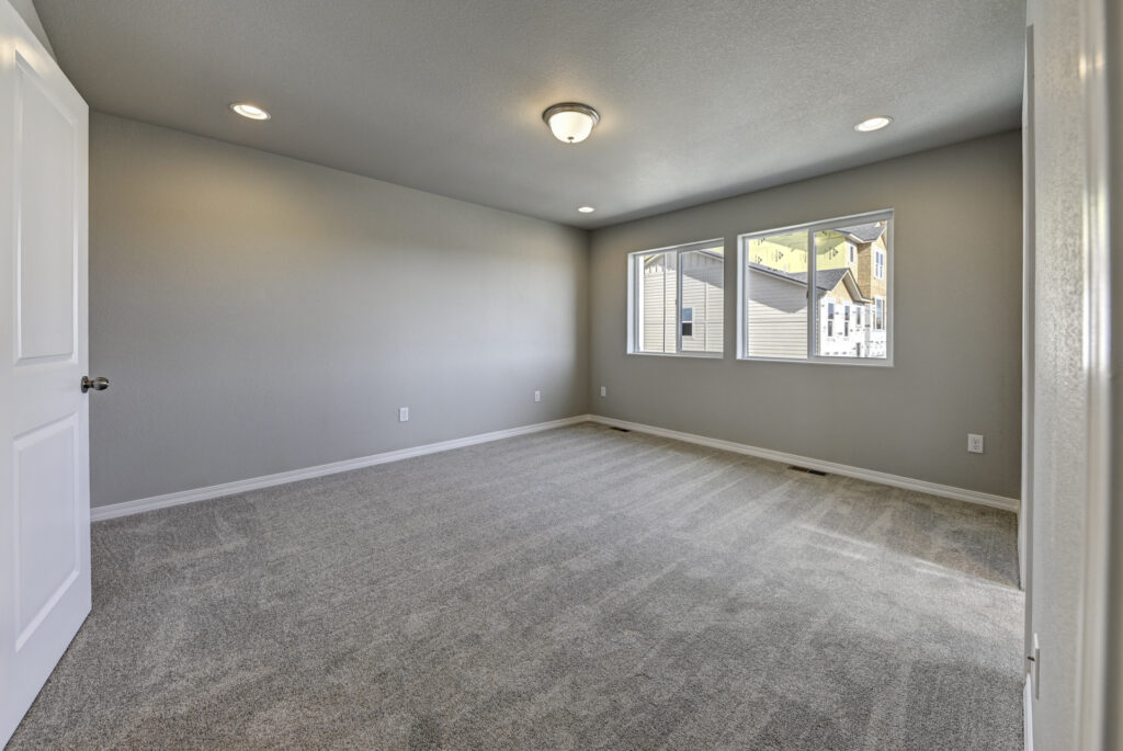 Carpeted bedroom with three windows looking out to neighboring houses.