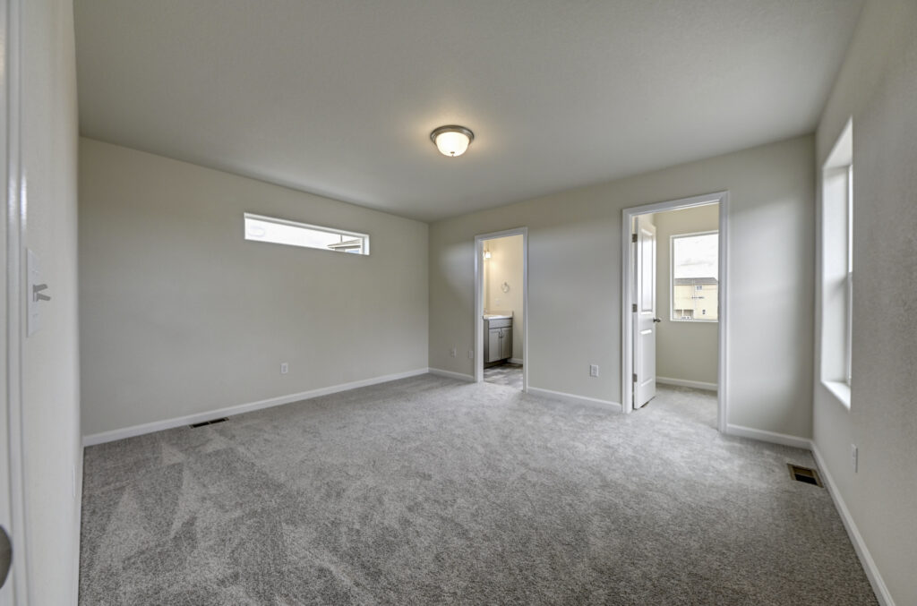 Empty carpeted bedroom with small horizontal window and two doorways leading to adjoining rooms.