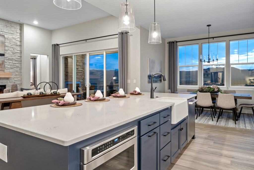 Open-plan kitchen island with blue cabinetry, white countertop, pendant lights, and living area beyond.