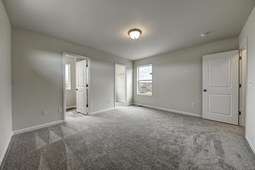Large empty bedroom with two doorways, closet opening, and a single ceiling light.