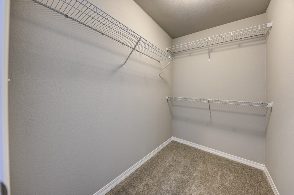Empty walk-in closet with beige carpet and white wire shelving on two walls.