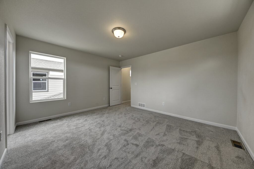 Empty rectangular room with carpet, one window, and an open door to a hallway.