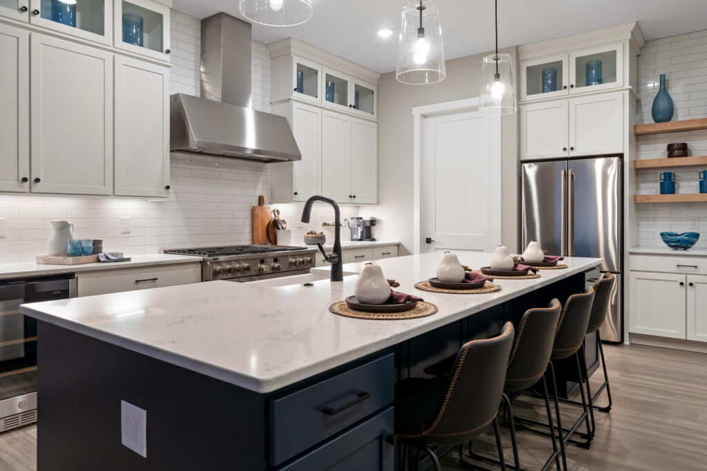 Modern kitchen with long island, white upper cabinets, stainless steel range hood and refrigerator.