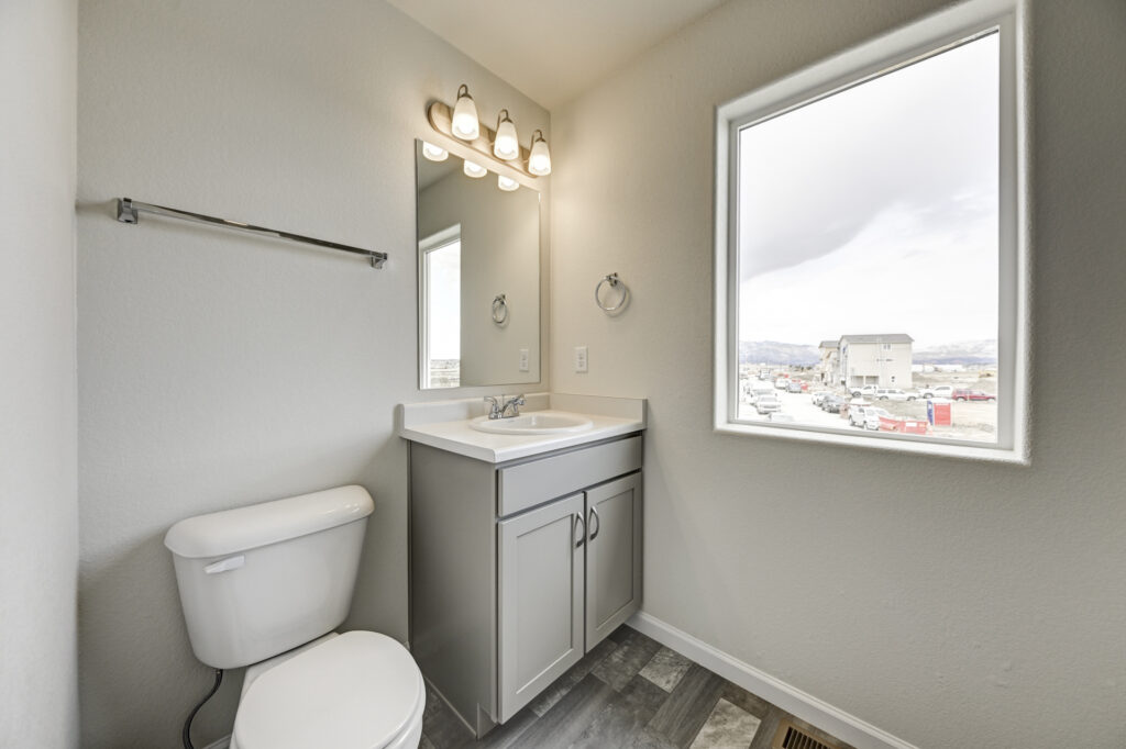 Small bathroom with vanity, mirror, toilet, and a window overlooking surrounding houses.