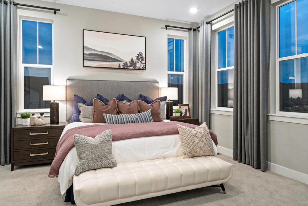 Staged bedroom with upholstered bed, layered pillows and blankets, bedside tables and floor-length curtains.