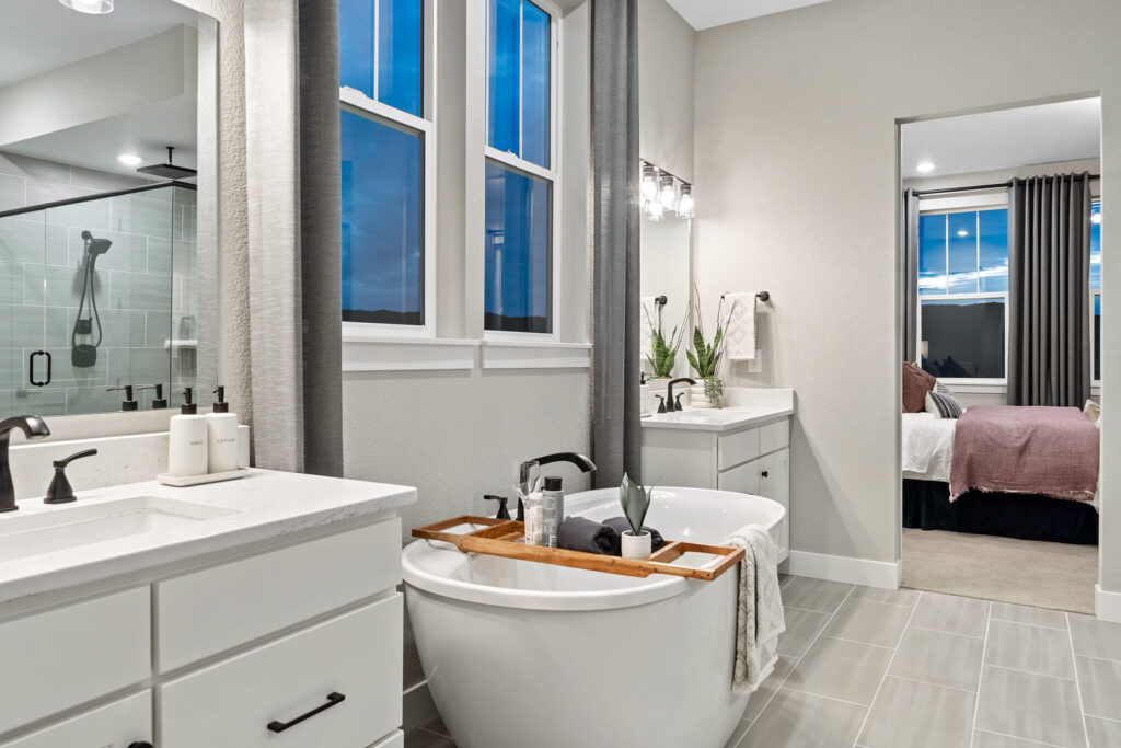 Bathroom interior with freestanding tub, dual vanities, and a view into the adjacent bedroom.