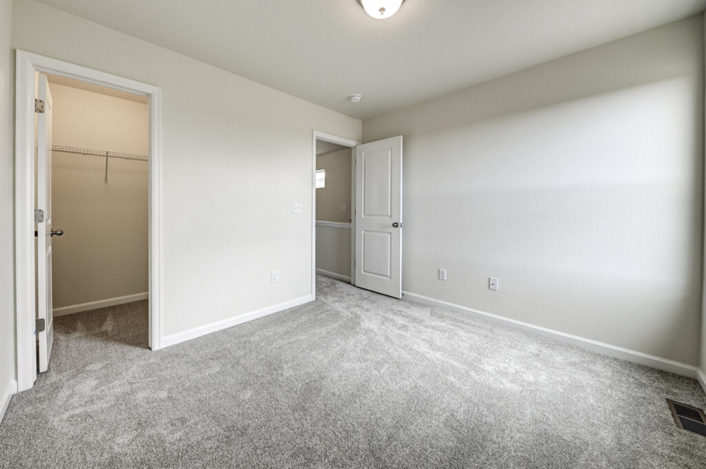 Empty bedroom showing an open door, closet doorway, and light gray carpeting.