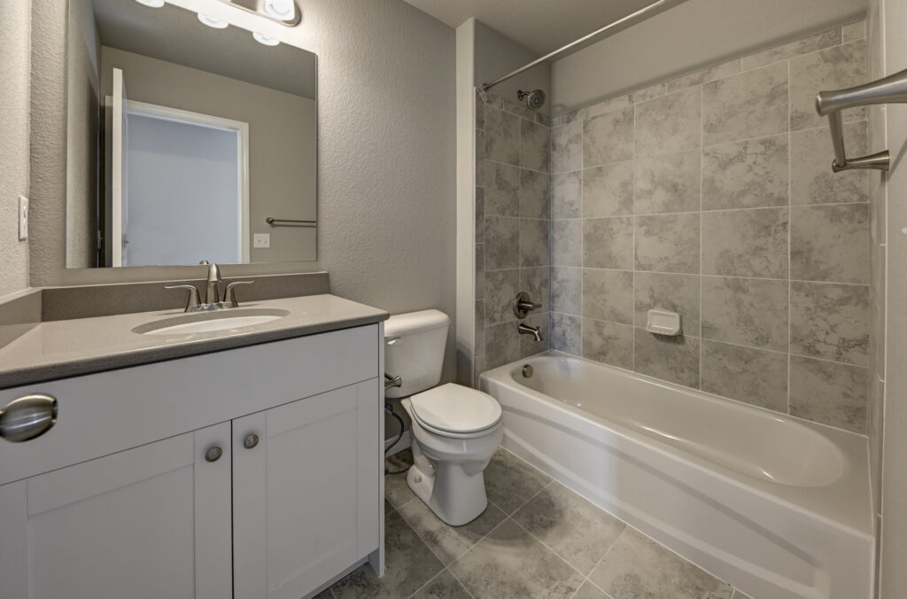 Small bathroom with vanity, toilet, and tub-shower combo with tiled surround.