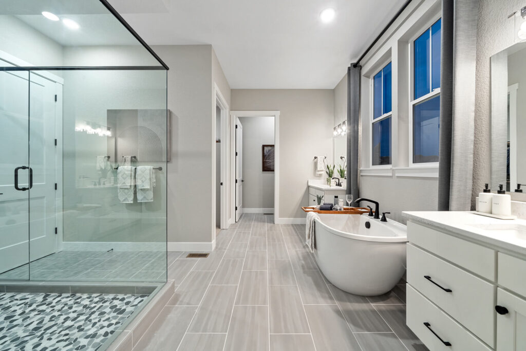 Wide-angle bathroom view showing large glass shower, freestanding tub, and long tiled floor.