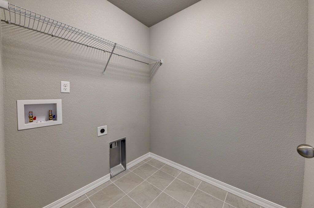 Empty laundry room with wall shelf, utility hookups, and tiled floor.