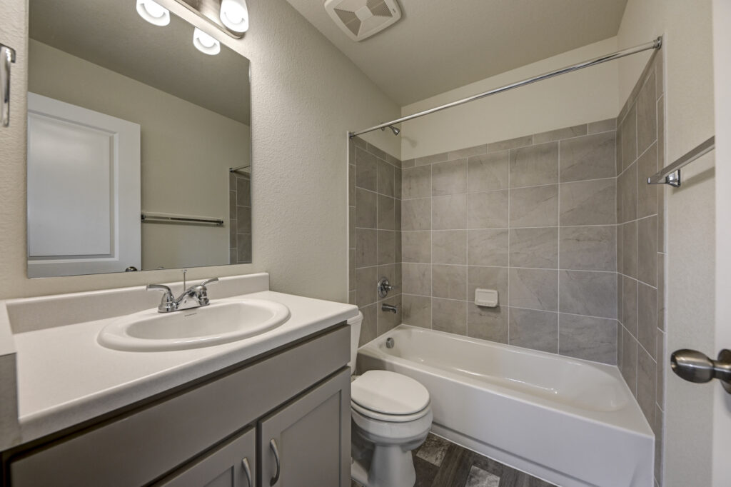 Bathroom with single sink vanity, mirror, toilet, and tiled bathtub-shower surround.