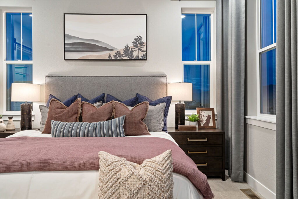 Close frontal view of bed headboard with layered pillows, bedside lamp, and framed art.