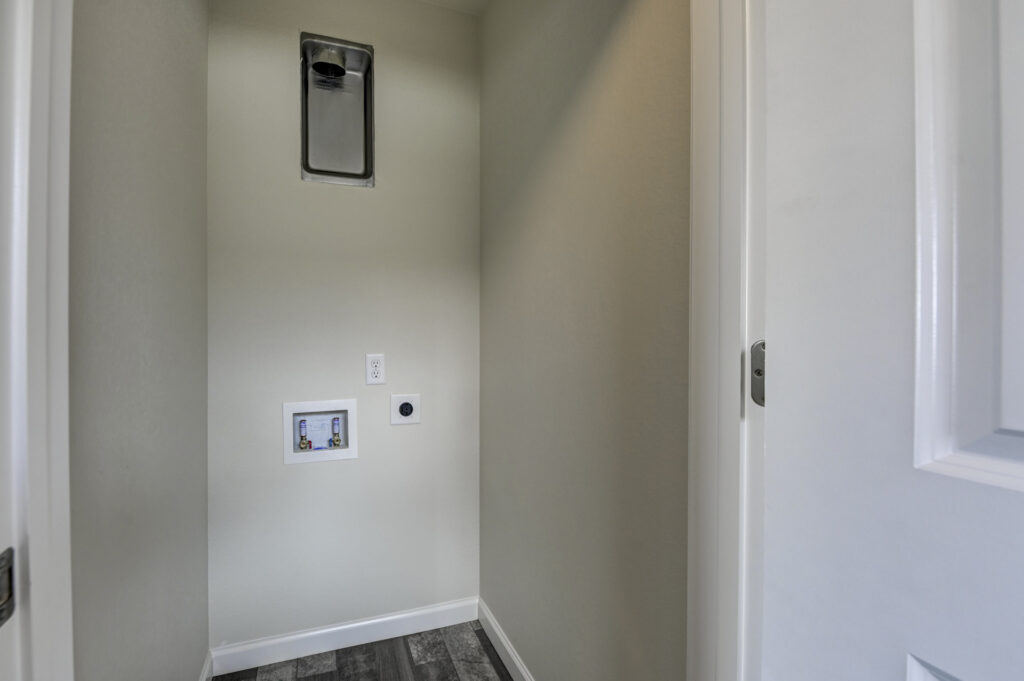 Small laundry nook with washer/dryer hookups, vent and electrical outlet, empty walls.