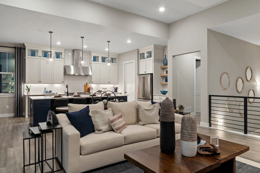 Open-plan living area with light sofa and kitchen in background under recessed lighting.