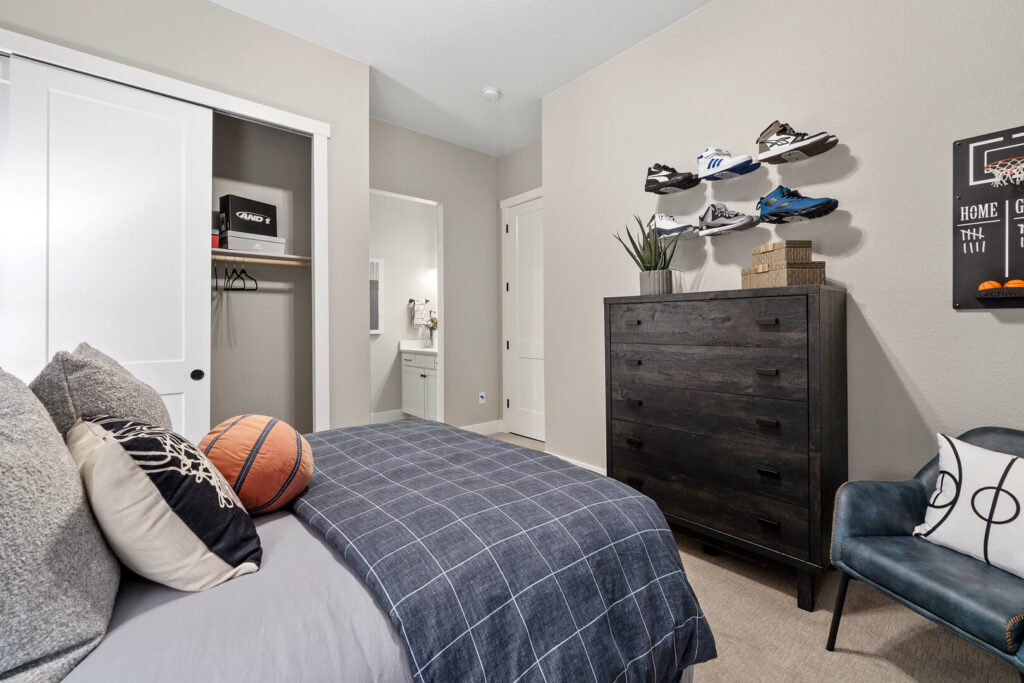 Bedroom view from foot of bed showing dresser, open closet, shoe display and a basketball on the bed.