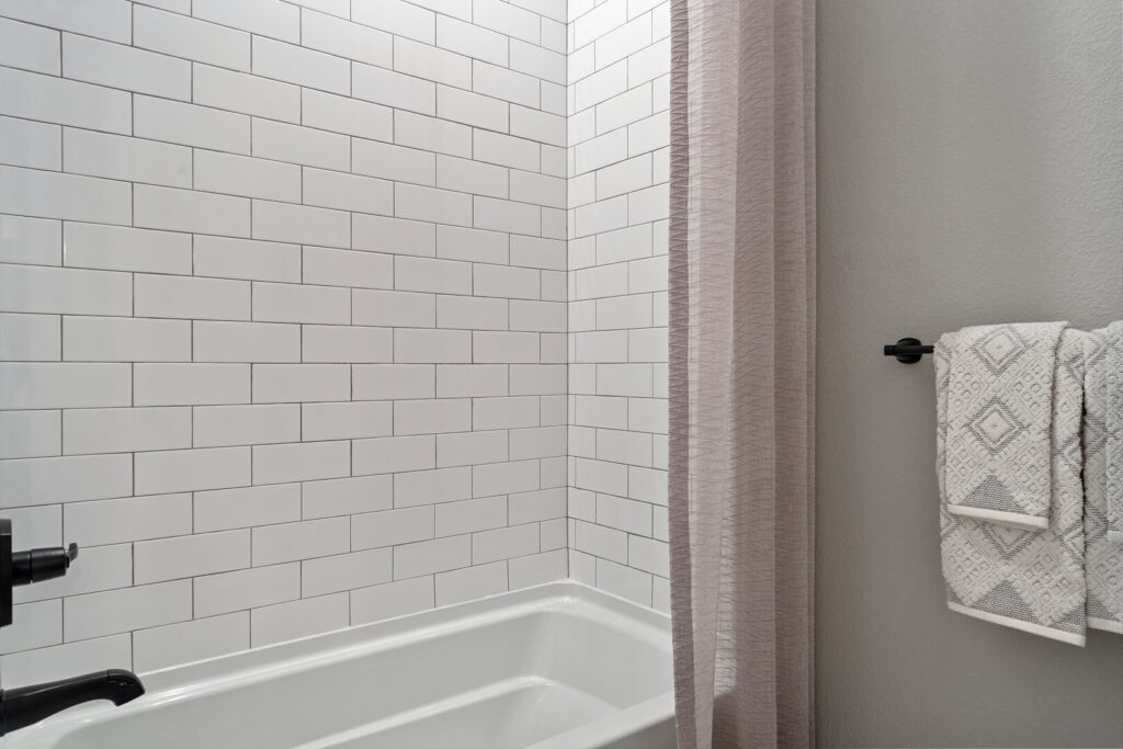 Tub and shower with white subway tile surround, dark faucet, and a pinkish shower curtain and towel rack.