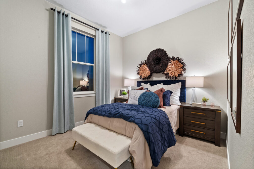 Neatly made bed in a small bedroom with blue bedding, decorative wall art, and nightstands.